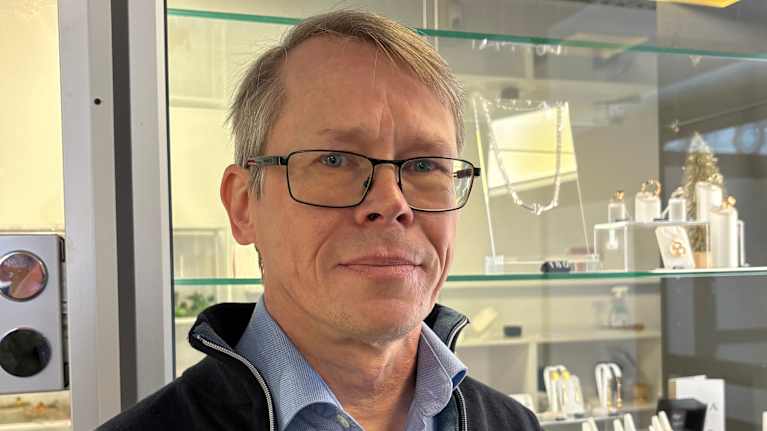 Mies katsoo kameraan taustalla kultakoruja vitriinissä.