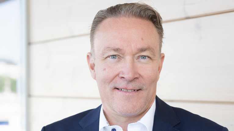 Kuvassa mies nojaa kaiteeseen puku päällä ja katsoo kameraan. Henkilökuva.