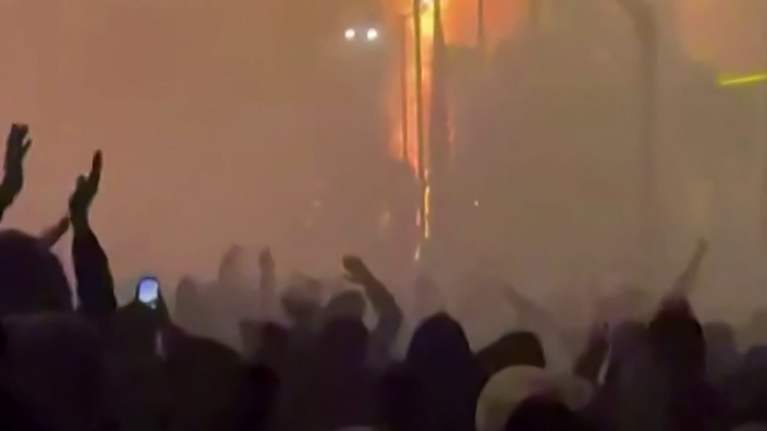 Mielenosoittajia Tehranissa, savua sakeana ilmassa, kaukana näkyy talo palamassa.