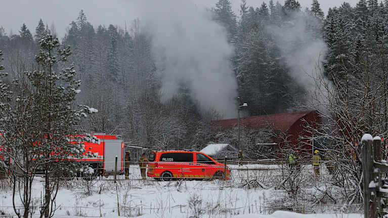 Paloauto talvisessa maisemassa taustalla nousee savua.
