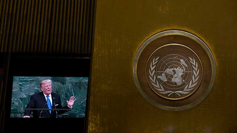 I förgrunden FN:s logo, i bakgrunden en tv-skärm där USA:s president Donald Trump syns talandes inför generalförsamlingen.