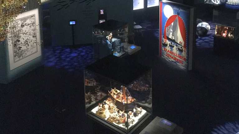 Näkymä Muumimuseon ylätasanteelta alas. Etualalla on pyrstötähteä esittävä helmiteos ja alhaalla näkyy pienoismaailmoja lasikuvuissaan.