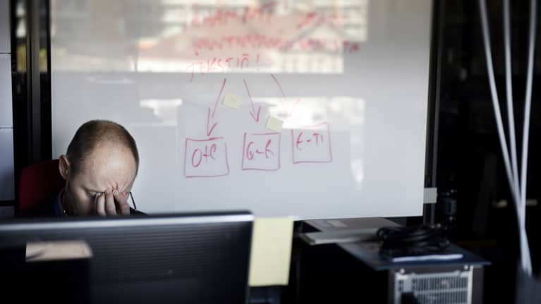 Työntekijä hieroo otsaansa työpöydän ääressä.