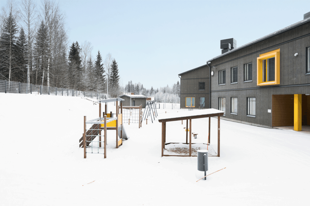 Leikkitelineitä lumisella pihalla.