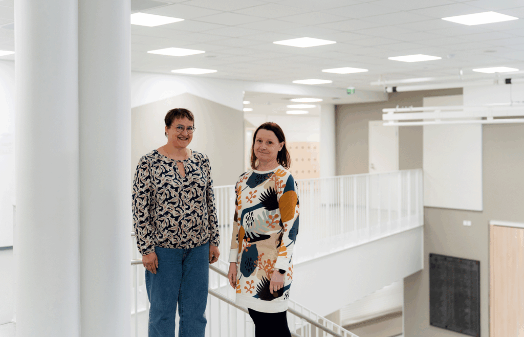 Kaksi henkilöä seisoo portaiden yläpäässä aulassa.