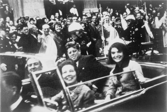 Kuva hetkeä ennen John F. Kennedyn salamurhaa. Presidenttiparin edessä istuvat kuvernööri John Connelly ja Nellie-vaimonsa. Kuvernööri loukkaantui luodeista vakavasti, mutta selvisi hengissä.