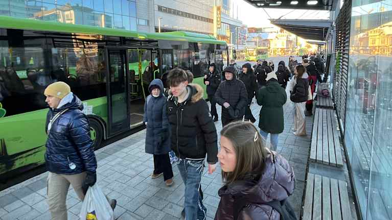 Toppatakkeihin pukeutuneita ihmisiä odottamassa linja-autoa bussipysäkillä.
