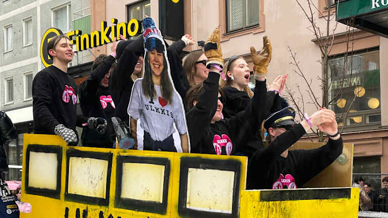 Kirkkaan keltainen mäenlaskukelkka, kyljessä teksti "Ulkkis" ja kyydissä riemuitsevia opiskelijoita.