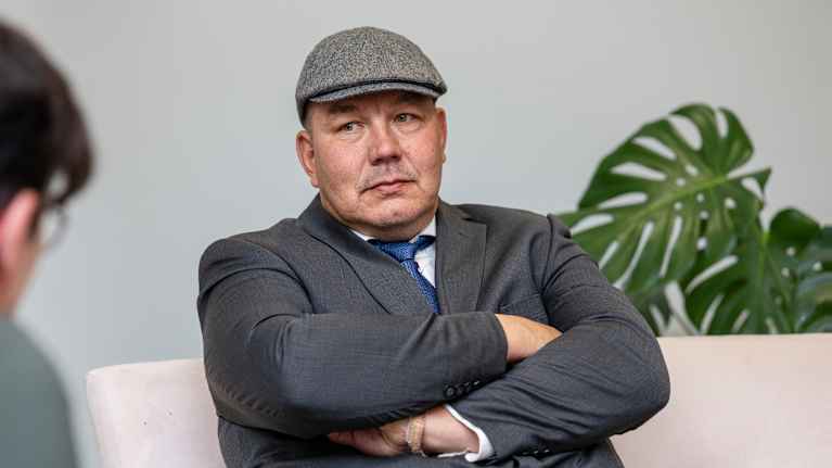 Juha Mäenpää istuu penkillä kädet puuskassa.