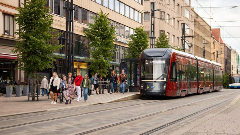 Ratikka pysähtyneenä pysäkille Tampereen Hämeenkadulla. Ihmisiä kävelee poispäin pysäkiltä.