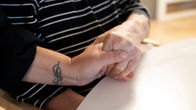 En yngre hand håller om en äldre hand. Det finns en tatuering på den yngres handled.