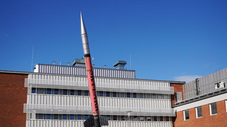 Talon pihalla on esillä pitkä raketti kirkkaan keväisen taivaan alla.