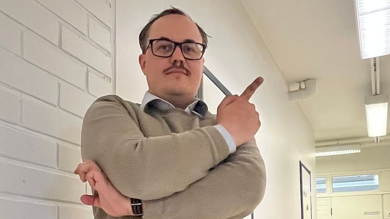 Henkilö seisoo käytävällä ja osoittaa sormellaan sivulle päin.