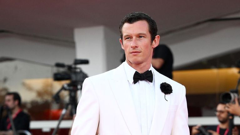 Callum Turner poseeraa punaisellamatolla.
