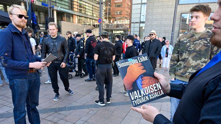Henkilö pitää kädessään lehteä jossa lukee "Sinimusta liike, Valkoisen työväen asialla". 