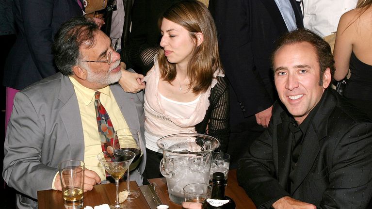 Francis Ford Coppola, Sofia Coppola ja Nicolas Cage istuvat pöydän ääressä juomien kanssa.