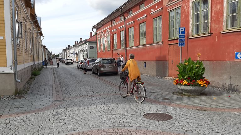 En cyklist med gul tröja cyklar på den stenlagda gatan mellan trähusen i Gamla Raumo.