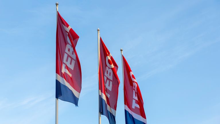 Kolme Teboil-merkkistä lippua liehuu sinistä taivasta vasten.