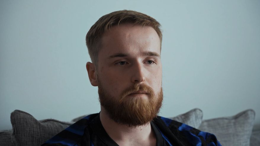 Nuori parrakas mies istuu sohvalla.