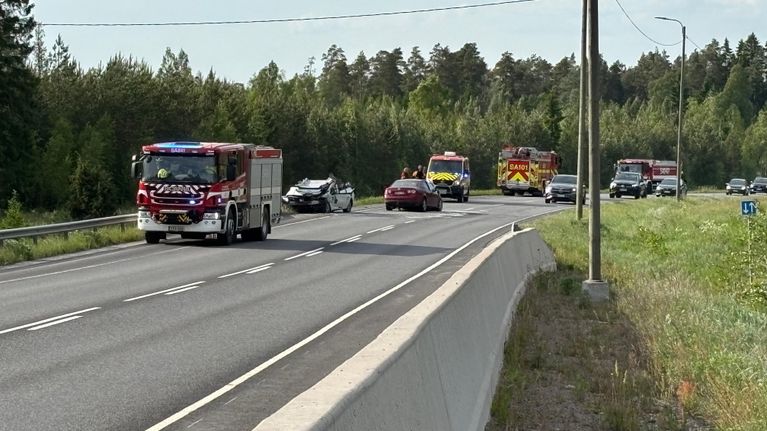 Onnettomuuspaikalla on pelastusajoneuvoja ja kaksi vaurioitunutta henkilöautoa. Toisella kaistalla ajaa henkilöautoja.