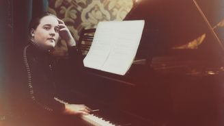 Tummapukuinen pianisti Astrid Joutseno istuu pianon äärellä ja katsoo kameraan. Nuottitelineellä on nuotti. Mustavalkokuva on värjätty.