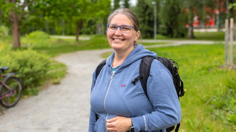 Maiju Salonen hymyilee kameralle iloisesti. Taustalla vehreää puistoa.