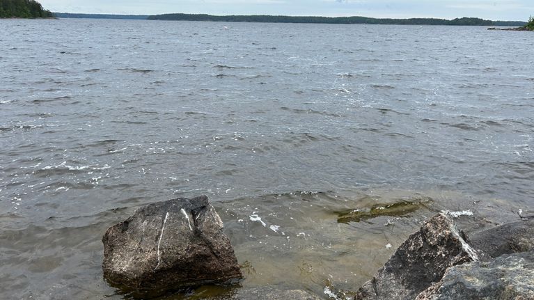 Rantakivikossa aaltoilevaa vettä, taustalla näkyy saaria ja pilvinen taivas.