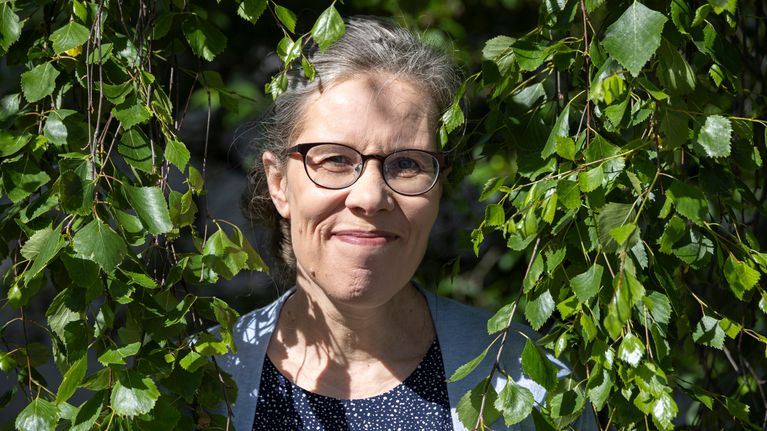Henkilö seisoo koivunoksien ympäröimänä ulkona, taustalla vihreitä lehtiä.