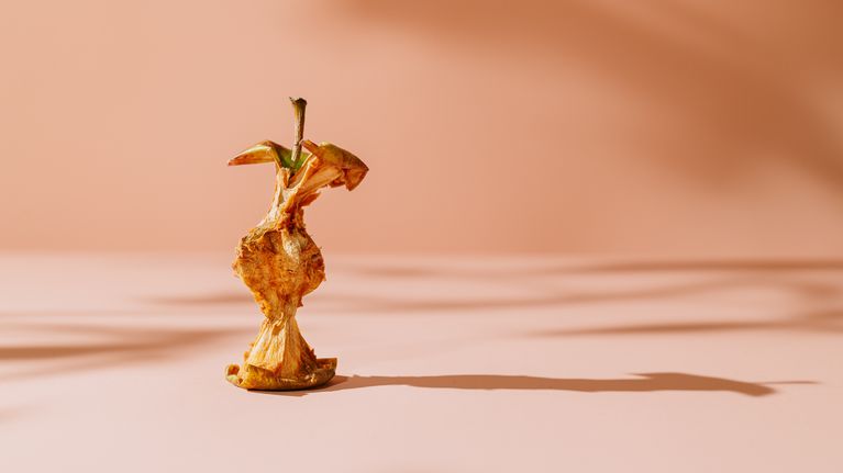 Omenan kara persikanvärisellä pinnalla, varjot heijastuvat taustalle.