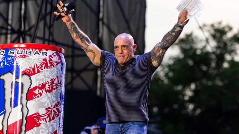 Joe Rogan pitää käsiään ilmassa esiintymislavalla.
