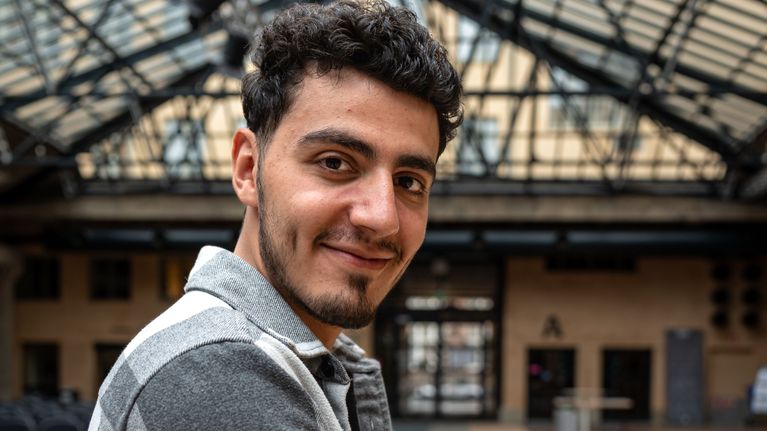 Näyttelijä Yussef Asab Alkhatib nojailee iloisena Teatterikorkeakoulun sisäpihalla tuolin selkämykseen.