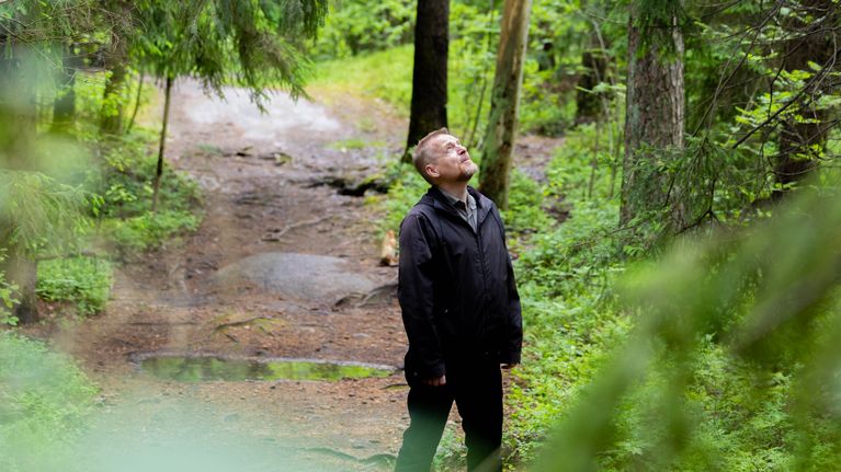 Janne Sivonen seisoo metsäpolulla ja katselee ylöspäin. Ympärillä on metsää.