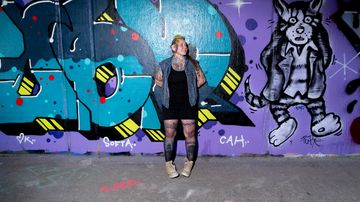 Nainen nojaa graffiteilla maalattuun seinään.