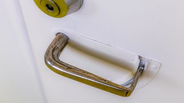 Valkoisessa ovessa hopeanvärinen ovenkahva ja yläpuolella pyöreä lukko, ei näkyvää tekstiä.