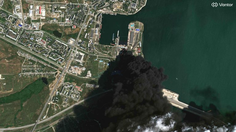 Satelliittikuva, jossa näkyy sankkaa mustaa savua nousemassa satama-alueella.