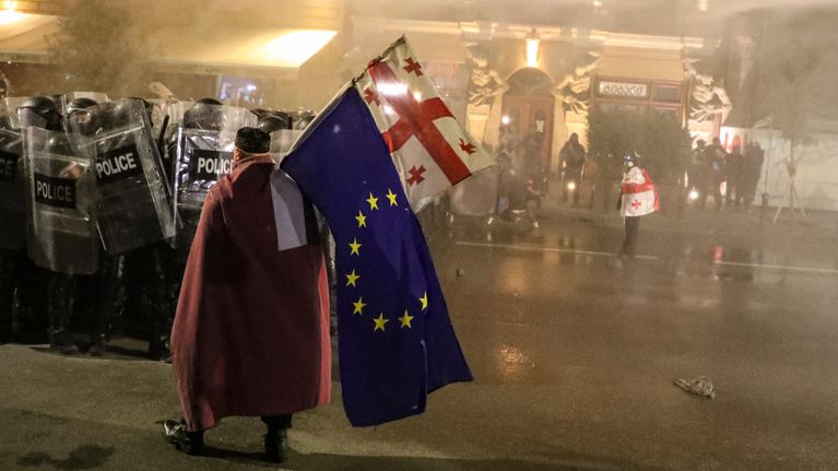 EU:n ja Georgian lippua kantava punatakkinen mielenosoittaja seisoo mellakkapoliisijoukon edessä.