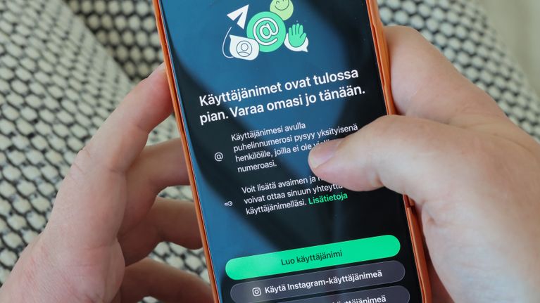 Kädet pitelevät matkapuhelinta, jossa näkyy Whatsappin uuden ominaisuuden käyttöönottomainos.