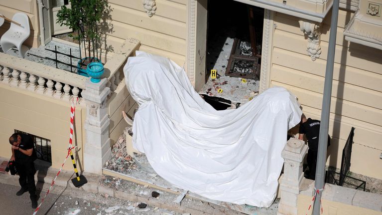Ett vitt skynke framför porten där bombdådet inträffade. Bakom syns blodfläckar och en bortsliten dörr. Poliser undersöker.