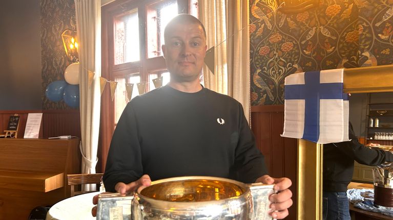 Kaljupäinen mies, Leijonien videovalmentaja Jukka Varmanen, seisoo ja pitää MM-pokaalia käsissään.