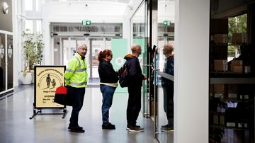Ihmiset seisovat jonossa kahvilan sisäänkäynnin ulkopuolella.