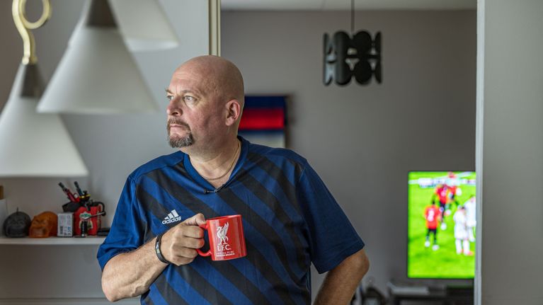 Mies juomassa kahvia ja katsomassa jalkapallopeliä kotonaan.