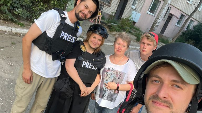 Kyseessä on kännykällä otettu ryhmäkuva, jossa on kolmen PRESS-suojavarusteisiin pukeutunutta ihmistä ja kaksi tavallisiin vaatteisiin pukeutunutta.