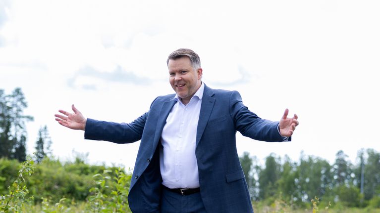 Siniseen pukuun pukeutunut mies seisoo keskellä vehreää peltoa.