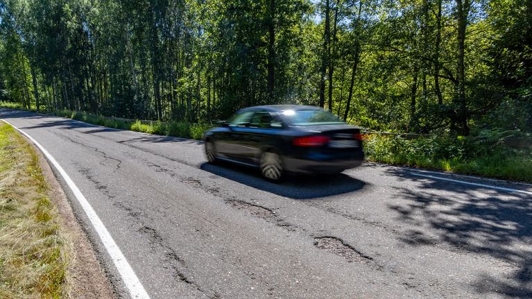 Auto ajamassa tiellä. Viereisellä kaistalla paljon kulumaa.