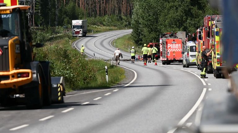 Useita pelastusajoneuvoja ja viranomaisia käänteisen S-mutkan kohdalla maantiellä, taustalla rekka-auto.