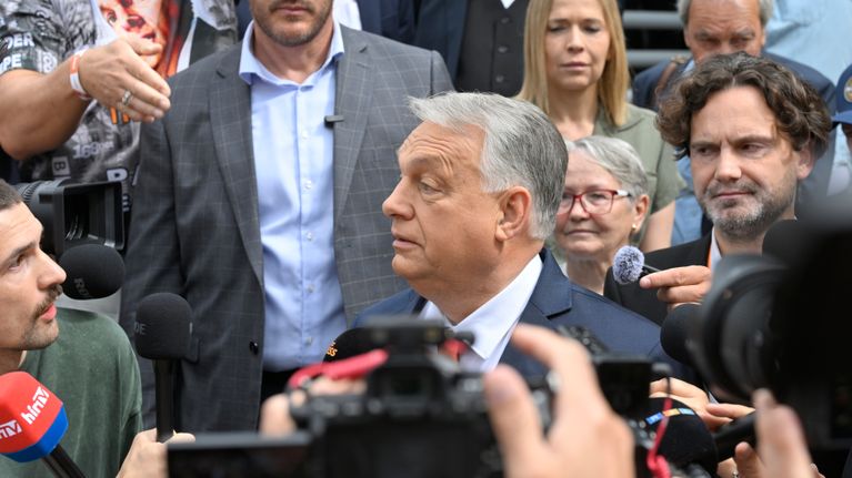 Orbán on toimittajien ympäröimänä tummassa puvussa, vaaleassa kauluspaidassa ja kravatissa.