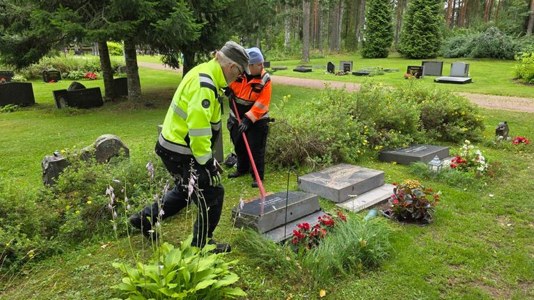 Kaksmi miestä nostaa työkalujen avulla kaatunutta hautakiveä.