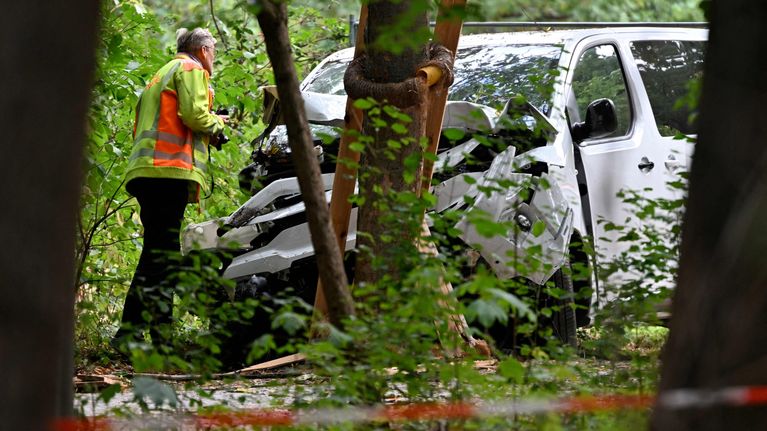Huomioväriseen takkiin pukeutunut ihiminen tarkastaa valkoista autoa, joka on ajanut puuta päin. Etualalla huomionauhaa.