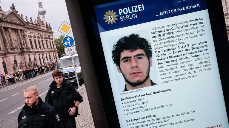 Kaksi poliisia seisoo kadulla, etualalla on poliisin etsintäkuulutus, jossa on miehen kuva ja saksankielistä tekstiä.