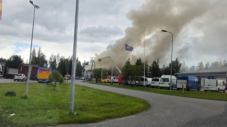 Rakennuksesta nousee savua, pihalla on pelastusajoneuvoja.